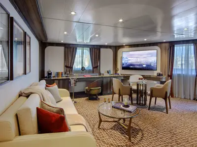 Blick in den großzügigen Wohnbereich einer eleganten Suite an Bord der Seabourn Venture mit Sitzecke, Fernseher und Schreibtisch.