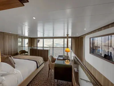 Blick in eine luxuriöse Suite an Bord der Seabourn Venture mit Bett, Schreibtisch und Aussicht auf eine arktische Gletscherlandschaft.