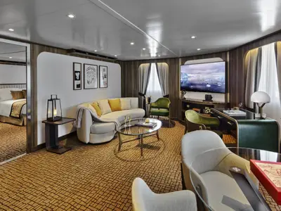 Ein Blick in eine elegant eingerichtete Suite an Bord der Seabourn Venture mit einem geschwungenen Sofa, Sesseln und einem Schlafzimmer im Hintergrund.