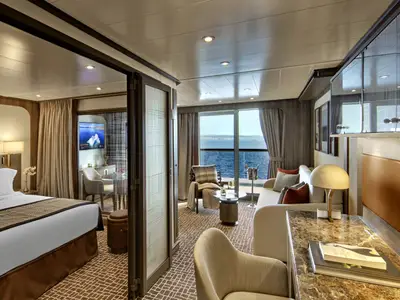 Blick in eine luxuriöse Suite an Bord der Seabourn Venture mit Schlafbereich, Wohnbereich und Balkon zum Meer.