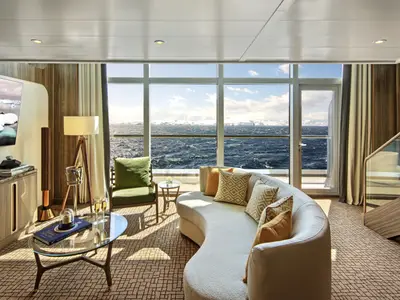 Das Wohnzimmer der Wintergarden Suite an Bord der Seabourn Venture mit modernem Sofa und Blick auf das eisige Polarmeer durch große Panoramafenster.