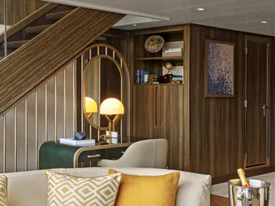 Ein eleganter Arbeitsbereich unter einer Holztreppe in einer Suite an Bord der Seabourn Venture mit beleuchtetem Spiegel und Schreibtischlampe.