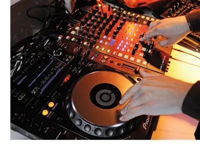 Ein DJ legt in der Abtanz Bar an Bord der Mein Schiff 1 auf. Nahaufnahme der Hände beim Bedienen des Mischpults und Plattenspielers. Verschiedene Knöpfe und Lichter sind zu sehen.
