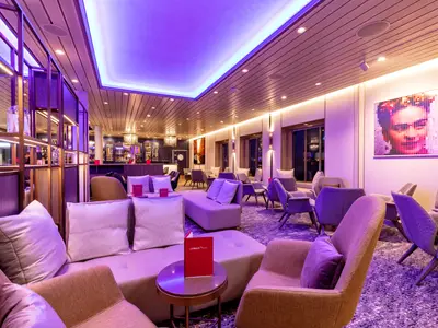 Innenansicht der LUMAS Bar an Bord der Mein Schiff 1. Modern und elegant gestaltet mit lilafarbenem Licht, gemuetlichen Sesseln, Sofas und einer Bar.