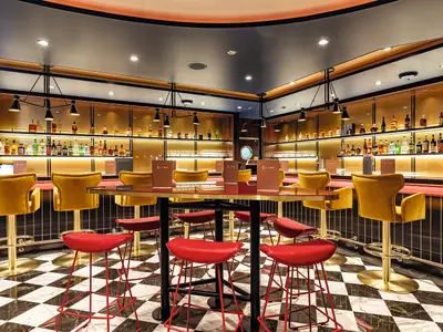 Blick in die stilvolle Schau Bar an Bord der Mein Schiff 1 mit einer Reihe von Spirituosen und eleganten Hockern in Gelb und Rot.