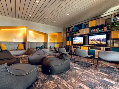 Gaming-Lounge an Bord der Mein Schiff 1. Zwei Bildschirme für Videospiele. Beanbags und Sitznischen mit Kissen. Bücher und Pflanzen schmücken den modern gestalteten Raum.