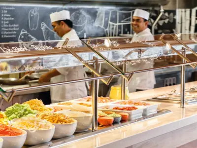 Im Buffet-Restaurant Anckelmannsplatz an Bord der Mein Schiff 1 bereiten Köche Gerichte frisch zu. Zahlreiche Schalen mit Nudeln, Gemüse und Fleisch stehen bereit.