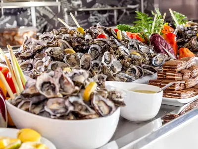 Ein üppiges Buffet mit vielen frischen Austern, Zitronen und Gemüse an Bord der Mein Schiff 1. Daneben stehen Schokoladenkuchenstücke und Saucen bereit.
