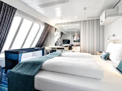 Helle Familienkabine Aussen auf der Mein Schiff 1. Sie zeigt zwei Einzelbetten, ein Babybett, Schreibtisch und grosse Fenster zum Meer.