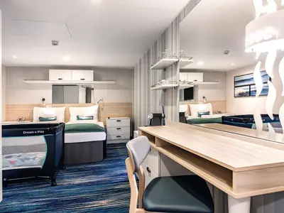 Eine helle Innenkabine an Bord der Mein Schiff 1 mit zwei Einzelbetten, einem Babybett und einem Holzschreibtisch. Moderne, funktionale Einrichtung mit blauem Teppich. Ideal fuer Familien.