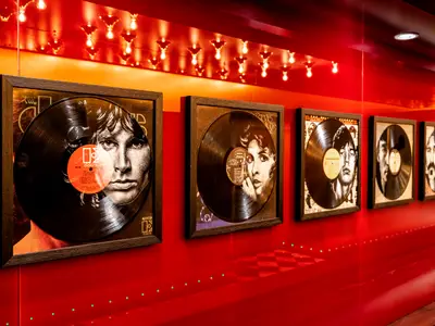 Gerahmte Schallplatten mit Musikerportraits an einer leuchtend roten Wand. Helle Lichter reflektieren von oben. Eine moderne Kunstinstallation an Bord der Mein Schiff 1.