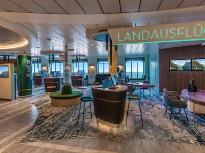 Modern eingerichteter Landausflugsbereich an Bord der Mein Schiff 1 mit Beratungs-Desks, Computern und Sitzbereichen. Helle Atmosphäre und Ausblick auf das Meer.