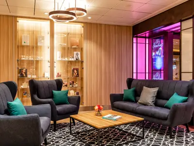 Moderne Lounge an Bord der Mein Schiff 1 mit dunklen Sesseln und Sofa, grünen Kissen, Holztisch und Vitrinen mit Schmuck. Neonlichter im Hintergrund.