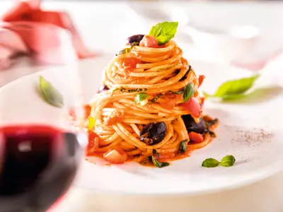 Appetitlich angerichteter Teller Spaghetti mit Tomatensauce, schwarzen Oliven und Basilikum an Bord der Mein Schiff 1. Im Vordergrund unscharf ein Glas Rotwein.
