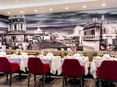 Elegantes Restaurant an Bord der Mein Schiff 1 mit gedeckten Tischen und roten Stühlen. Die Wand ist mit einem großflächigen schwarz-weißen Wandbild einer historischen Stadtlandschaft verziert.