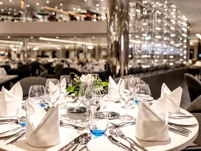 Festlich gedeckter Tisch mit Servietten und Gläsern im Restaurant Atlantik Klassik an Bord der Mein Schiff 1. Im Hintergrund schimmernde Lichtinstallation und weitere Tische.