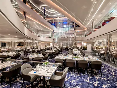 Das elegante Atlantik - Klassik Restaurant an Bord der Mein Schiff 1 mit zahlreichen gedeckten Tischen und einem mehrstufigen Design mit großer Lichtinstallation in der Mitte.