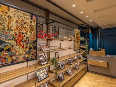 Modernes Tattoo Studio an Bord der Mein Schiff 1. Holzregale präsentieren gerahmte japanische Tattoo-Kunstwerke. Eine Rezeption und blaue Wände sind im Hintergrund sichtbar.
