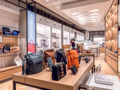 Ein heller, moderner Einkaufsbereich mit Regalen voller Handtaschen in verschiedenen Farben und Auslagen mit Uhren der Marken Guess und Fiorelli an Bord der Mein Schiff 1.