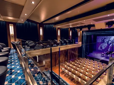 Elegante Schaubühne an Bord der Mein Schiff 1 mit Bühne, Flügel und LED-Wand (Sterne/Bäume). Sitzreihen im Parkett und Sessel auf der Empore sind sichtbar.