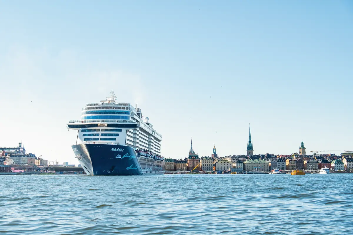 Die Mein Schiff 2 fährt auf blauem Meer an einer historischen Skyline mit vielen Kirchtürmen vorbei. Blauer Himmel.