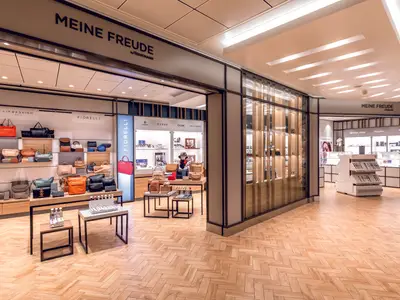Blick in einen Shop an Bord der Mein Schiff 2, der Handtaschen und Accessoires wie Geldbörsen und Düfte präsentiert. Der Boden ist mit einem hellen Holzparkett im Fischgrätmuster ausgelegt.