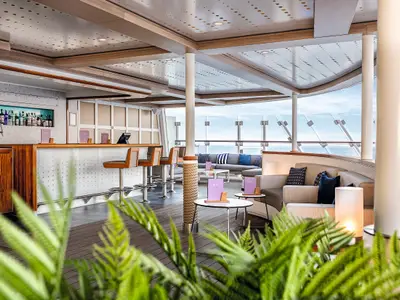 Einladende Innenansicht einer modernen Lounge und Bar an Bord der Mein Schiff 2. Der Raum bietet bequeme Sitzbereiche und einen Barbereich mit Barhockern. Eine breite Fensterfront ermöglicht einen Panoramablick auf das Meer.