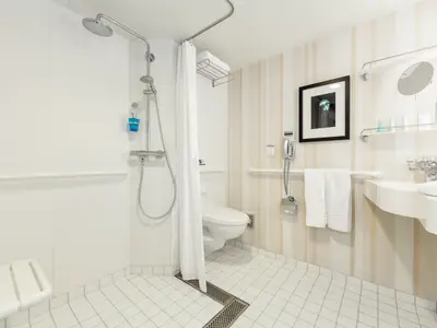 Barrierefreies Badezimmer an Bord der Mein Schiff 2. Es zeigt eine begehbare Dusche mit Duschsitz und Haltegriffen. Ein WC, Waschbecken und Spiegel sind ebenfalls integriert. Helles, funktionales Design.