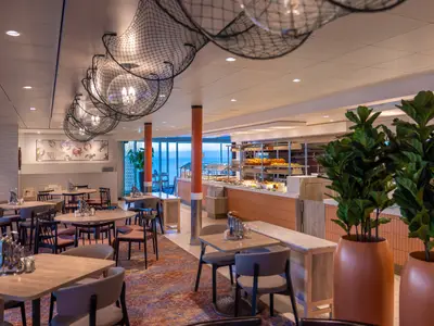 Modernes Buffetrestaurant Fischmarkt an Bord der Mein Schiff 2, mit Tischen, Buffettheke voller Speisen und Meerblick. Deckenleuchten als Fischernetze gestaltet.