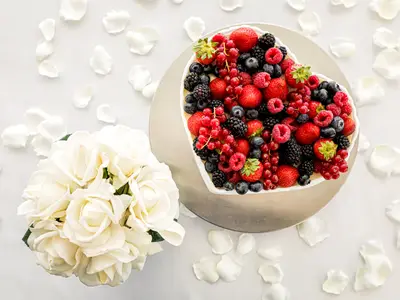 Vogelperspektive auf eine herzförmige Fruchttorte mit Beeren, umgeben von einem Rosenstrauß und Blütenblättern als Hochzeitsdekoration an Bord der Mein Schiff 2.