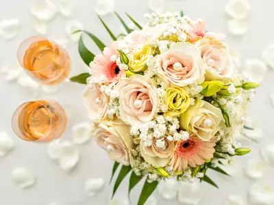 Romantische Hochzeit an Bord der Mein Schiff 2. Bunter Blumenstrauss mit Rosen, Schleierkraut, Perlen. Zwei Sektgläser und weisse Blütenblätter auf hellem Grund.
