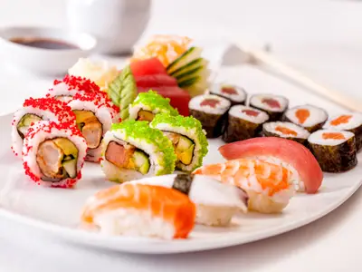 Mein Schiff 2: Eine Sushi- und Sashimi-Platte mit Maki-Rollen, Nigiri und rohem Fisch auf weissem Teller. Sojasauce und Essstäbchen im Hintergrund.