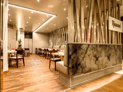 Innenansicht des Hanami Restaurants an Bord der Mein Schiff 3 mit langen Holztischen, gepolsterten Stühlen und Bänken. An der Wand befindet sich ein stilisiertes Gitter, dahinter eine weiße Neon-Leuchtreklame mit dem Schriftzug "Hanami Japanische Küche".