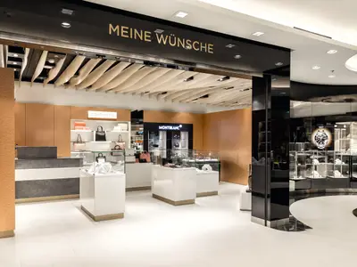 Innenansicht einer luxuriösen Boutique auf der Mein Schiff 3, die Handtaschen, Uhren und Schmuck in Glasvitrinen präsentiert. An der Decke hängt ein geschwungenes Design.