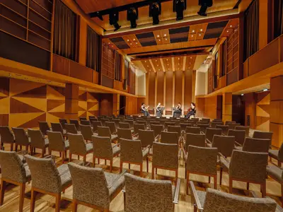 Blick in einen leeren Konzertsaal der Mein Schiff 3. Auf der Bühne sitzen vier Frauen mit Streichinstrumenten und Notenständern. Der Saal ist holzgetäfelt mit geometrischen Mustern und Reihen von Stühlen.