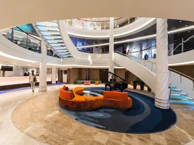 Das moderne Atrium der Mein Schiff 3 mit mehreren Etagen. Unten ist eine Rezeption, eine Piano-Bar und eine bogenförmige Couch. Treppen und Gänge führen nach oben.