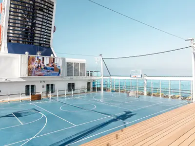 Blick auf das Außendeck der Mein Schiff 3 mit einem blauen Basketballfeld und Volleyballnetz. Im Hintergrund ist das blaue Meer zu sehen.