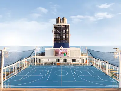 Blick vom Heck der Mein Schiff 3 auf das Sportdeck mit blauem Basketballfeld und dem Meer im Hintergrund unter einem klaren Himmel.
