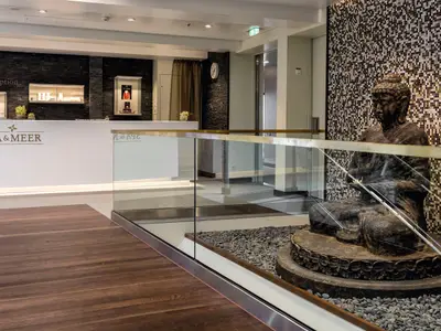 Die Rezeption des „SPA & MEER“-Bereichs auf der Mein Schiff 3 mit schwarzer Schieferwand, Vitrinen und einer Buddhastatue hinter einer Glasbalustrade.