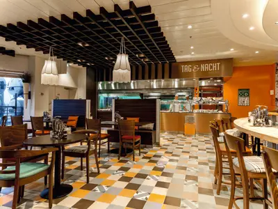 Innenansicht des "Tag & Nacht Bistro" auf der Mein Schiff 4 mit Selbstbedienungsbuffet, Tischen, Stühlen, Barhockern und Blick nach draußen.