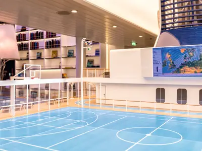 Ein detailliertes Modell des Schiffsinneren von Mein Schiff 4. Im Vordergrund ein blauer Basketballplatz. Im Hintergrund Regale und Bildschirme mit einer Europakarte.