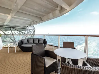 Ein breiter Balkon auf der Mein Schiff 5 mit bequemen Rattanmöbeln, darunter ein Sofa, zwei Sessel und ein Tisch, der Blick fällt auf das offene Meer.