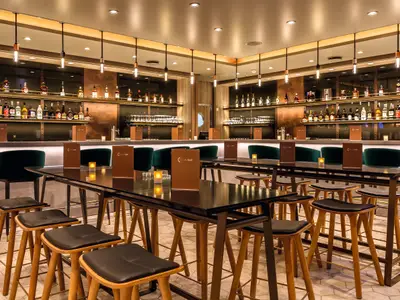 Eine elegante Bar an Bord der Mein Schiff 6. Die Theke ist mit Flaschen und Gläsern bestückt. Davor stehen hohe Tische mit dunklen Stühlen und Menükarten.