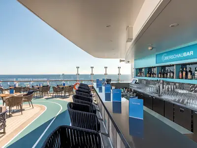 Ueberschau Bar auf der Mein Schiff 6. Aussenbar mit Barhockern, Tischen und stylischem Deck-Design mit Meerblick unter blauem Himmel. Ohne Personen.