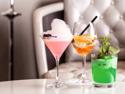 Drei kunstvolle Cocktails, pink, orange, gruen, in einer Bar an Bord der Mein Schiff 6. Der pinke hat eine Schaumkrone.