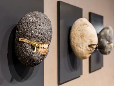 Kunst auf der Mein Schiff 6: Eine graue Steinskulptur mit Reißverschluss, der menschliche Zähne zeigt. Zwei weitere, unscharfe Skulpturen sind im Hintergrund zu sehen.