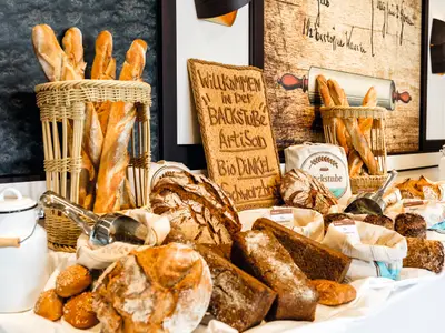 Einladendes Brot-Buffet an Bord der Mein Schiff 6 mit knusprigen Baguettes, dunklem Brot, Brötchen und einem 'Artisan'-Schild. Metallzangen liegen bereit.