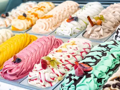 Eine farbenfrohe und verlockende Auswahl an Eiscremesorten, präsentiert in einer Kühltheke an Bord der Mein Schiff 6. Die cremigen Eissorten sind mit Früchten und Saucen dekoriert.