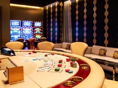 Ein luxuriöses Casino an Bord der Mein Schiff 6. Zu sehen ist ein Blackjack-Tisch mit Spielchips, Kartendealer-Schuh und Kartendealer-Ablage. Im Hintergrund leuchten zahlreiche Spielautomaten.