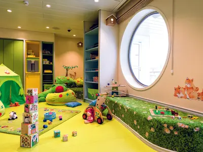 Heller Kinderbereich an Bord der Mein Schiff 6 mit Spielzelt, Bauklötzen, Sitzsäcken und Spielteppich. Großes Bullauge, Fuchs-Motive an der Wand.